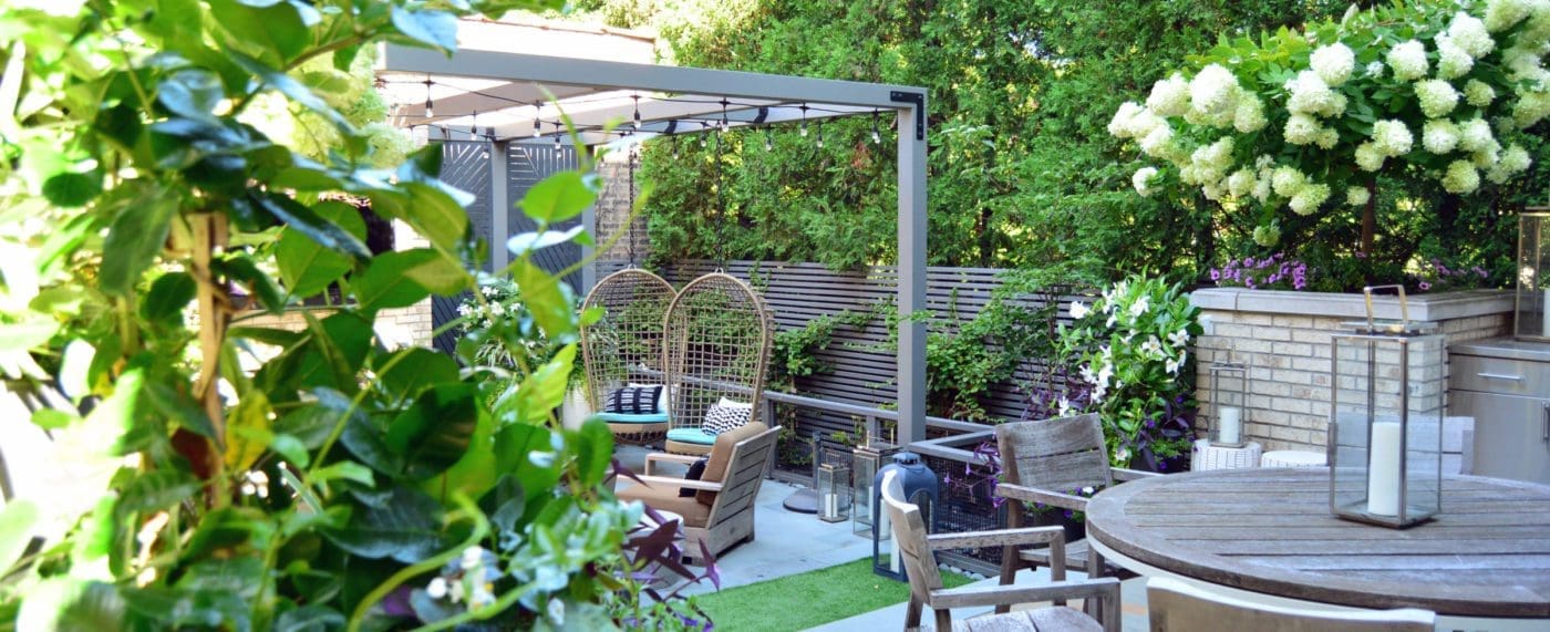 Outdoor kitchen with a grill, round table for dining, and a sitting area in an abundance of greenery.