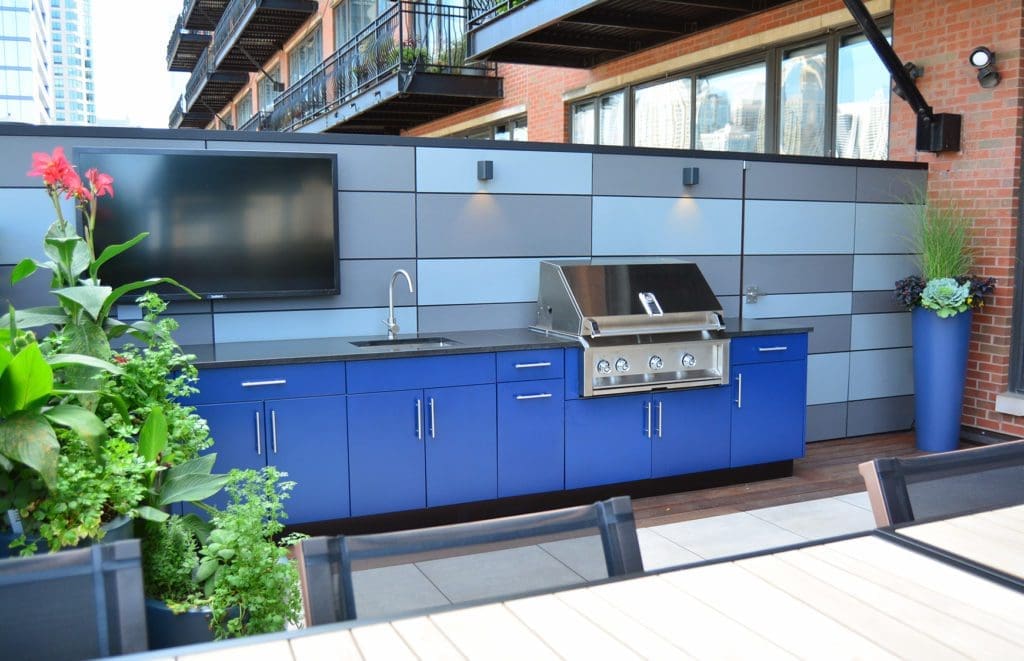 Blue cabinets and grill at outdoor kitchen with a flat screen mounted television.