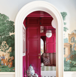 View into a doorway of a seating area with pink walls and beautiful intricate wallpaper.