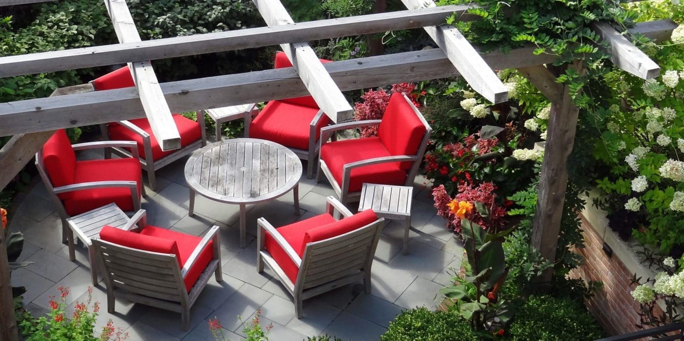 Pergola with a round dining table and chairs with red cushions.