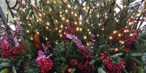 Winter floral display in a container with lighted branches.
