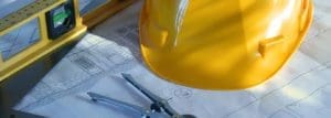 Yellow hard hat on top of drawn landscaping plans and a level.
