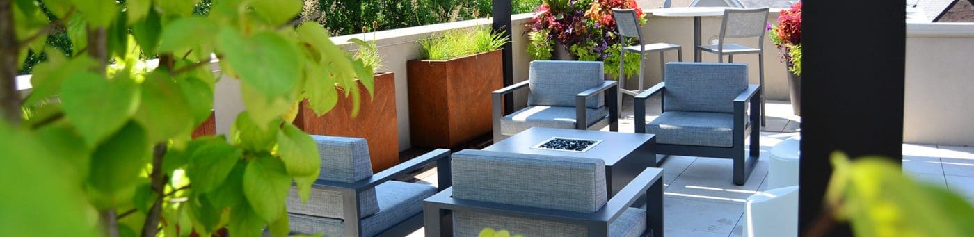 Outdoor roof deck with patio chairs, plants, and a square gas fire pit.