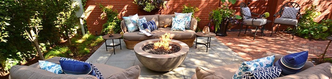 Outdoor patio area with couches, chairs, and a round gas fire pit.