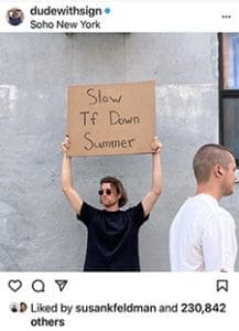 Dude with sign that says Slow Tf Down Summer.