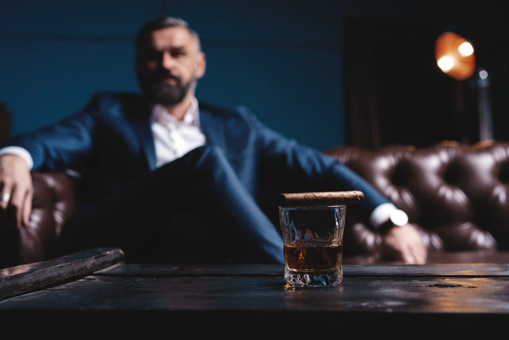 Portrait of handsome elegant mature man with cigar and a glass whiskey in a dark room